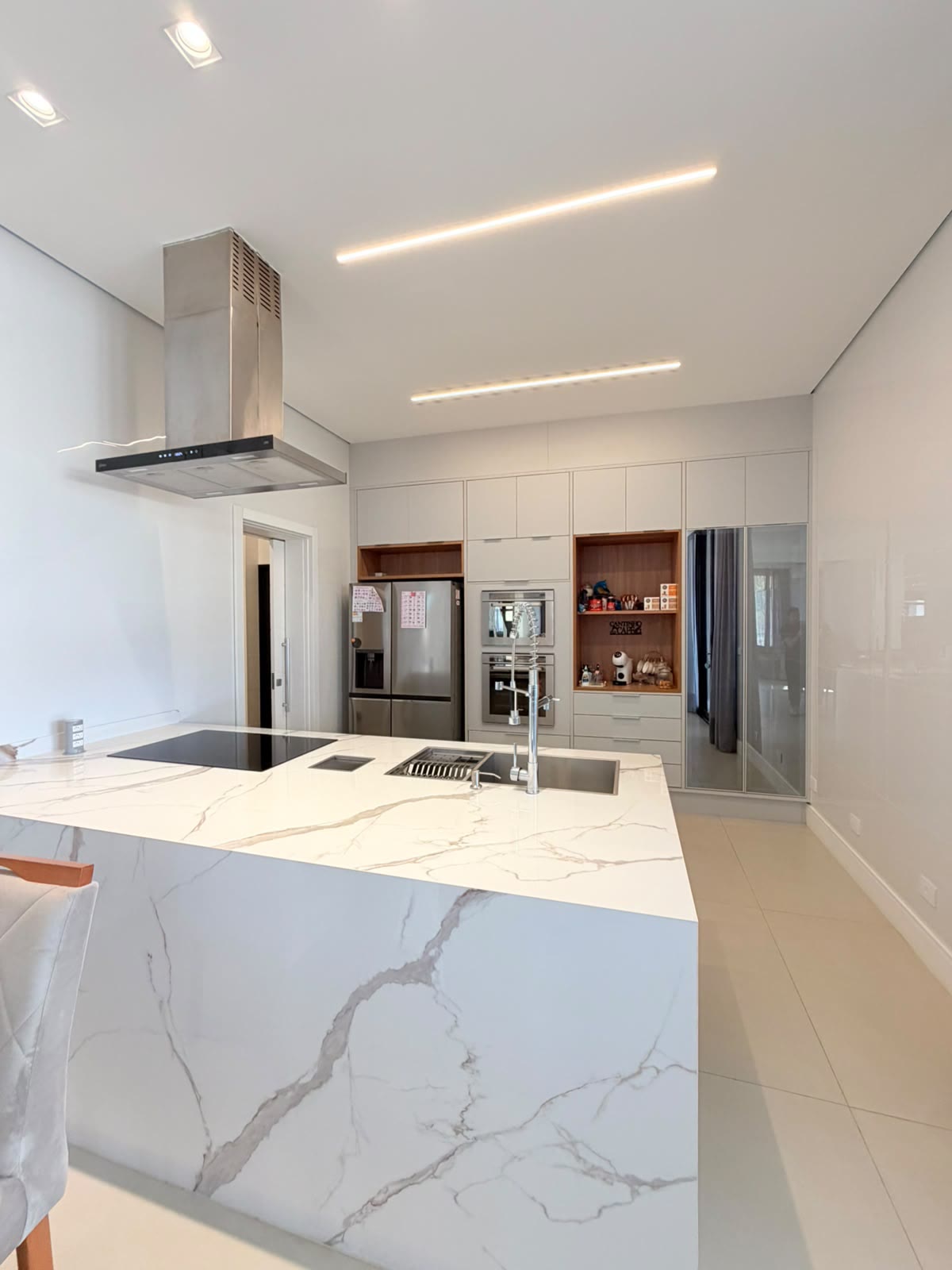 Cozinha com ilha revestida em lâmina de mármore, cooktop e coifa
