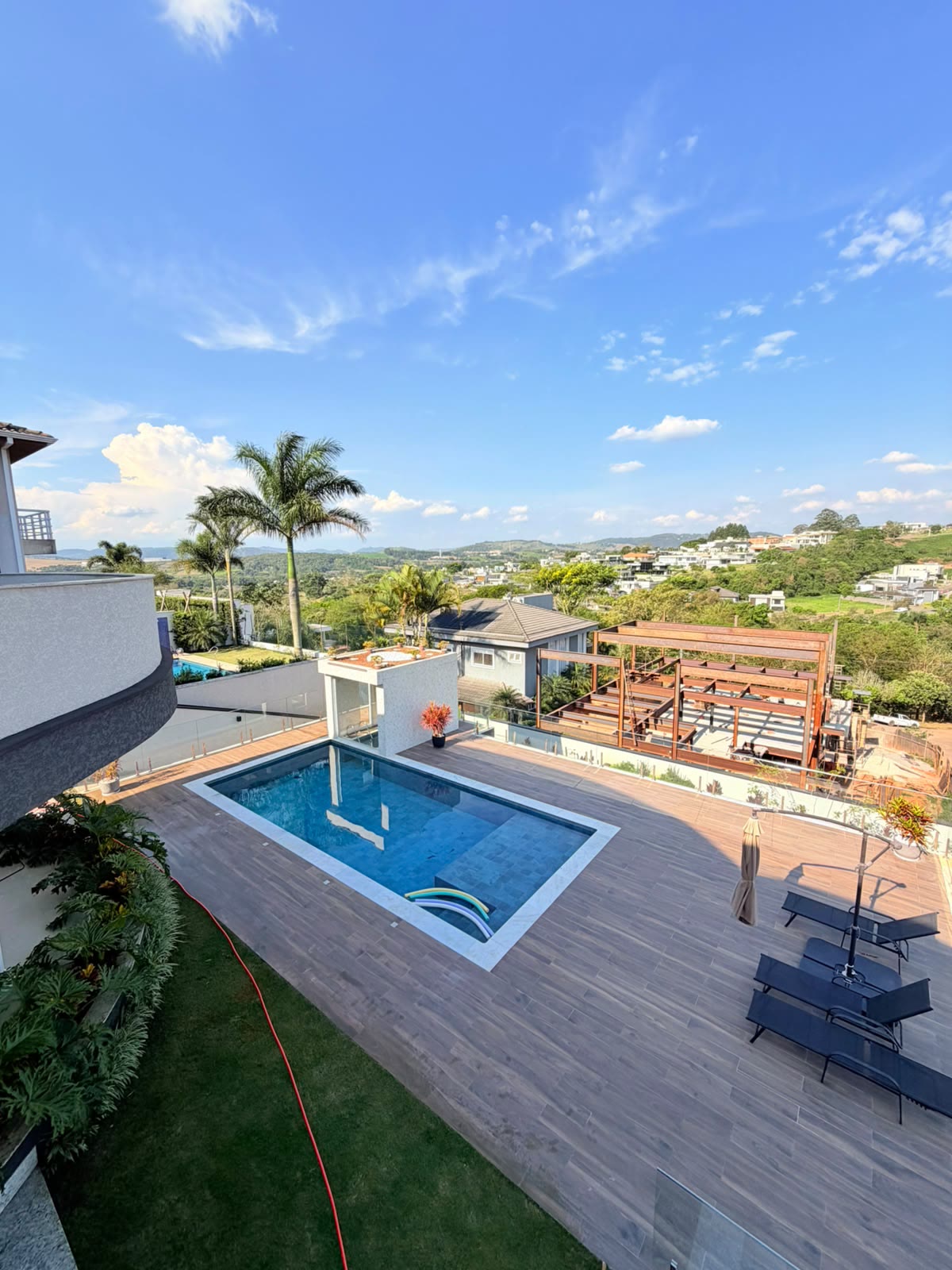 Piscina, deque de madeira e gramado sob céu azul