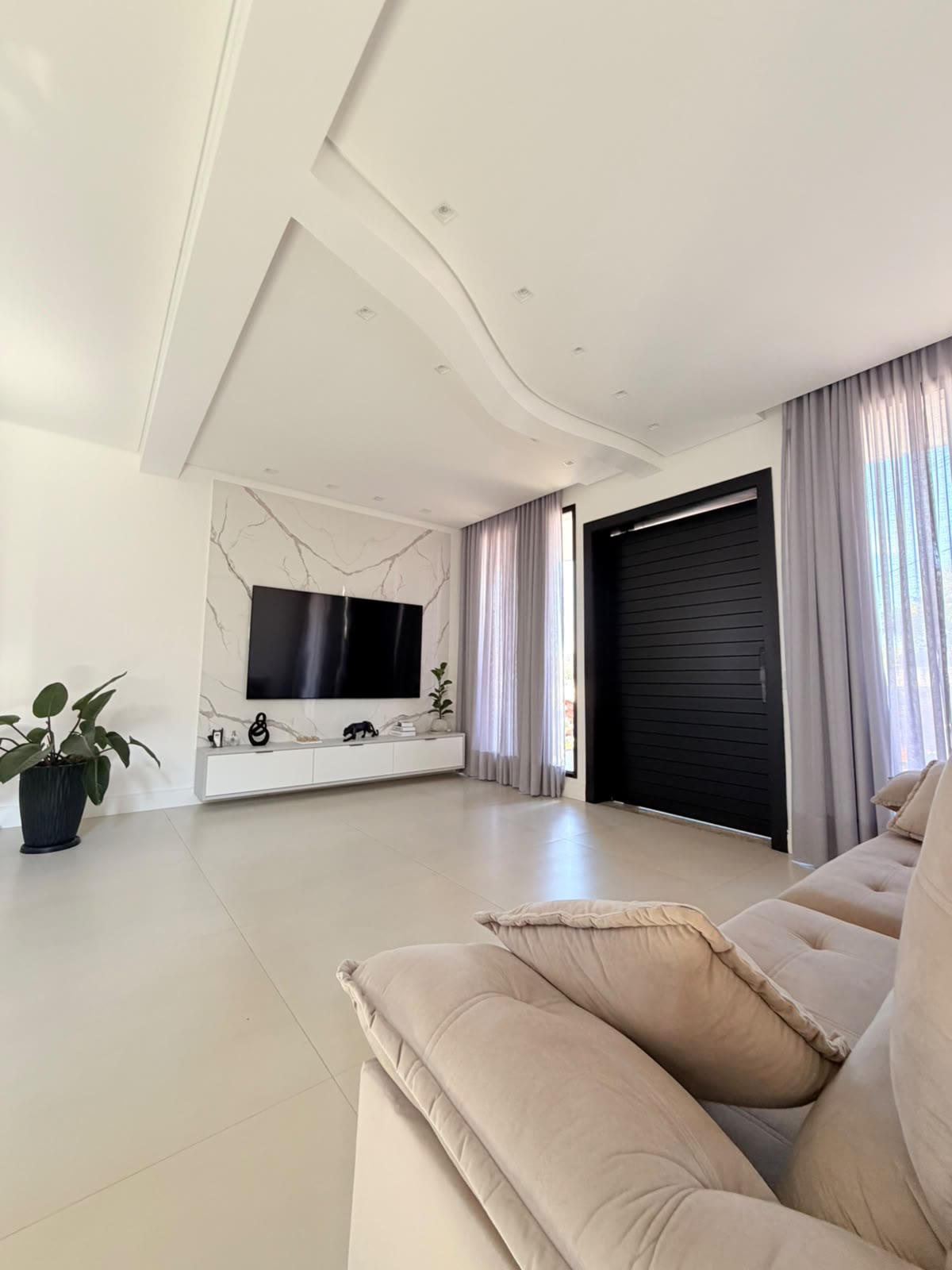 Sala de estar com sofá, painel de TV e grandes aberturas